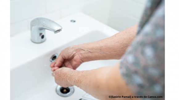 Persona mayor lavándose las manos en un lavabo con grifo electrónico.