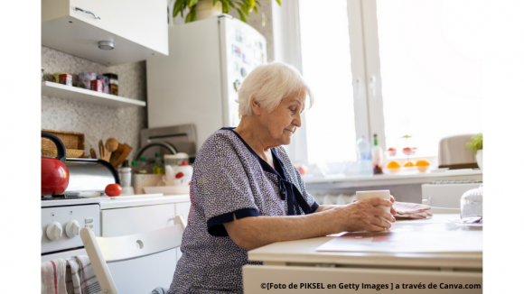 Mujer mayor sentada en la mesa de la cocina con un café en la mano.